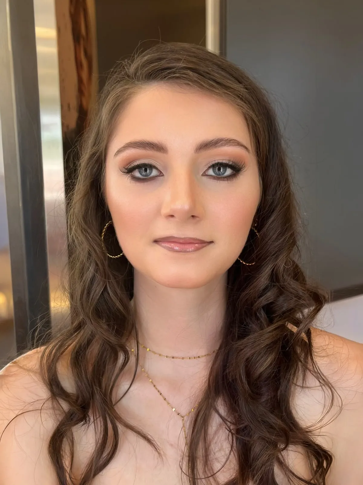 Dieselbe junge Frau mit Abend-Make-up: Smokey-Akzent, glänzende Lippen, weiche Locken und goldene Creolen