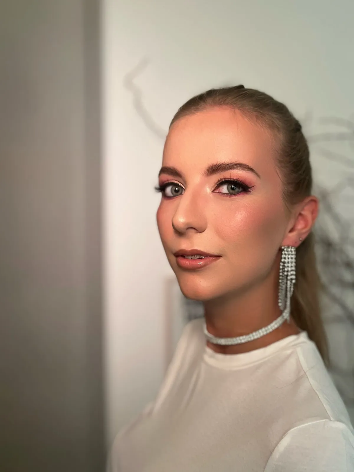 Dieselbe blonde Frau mit festlichem Abend-Make-up in Rosé und Strass-Schmuck