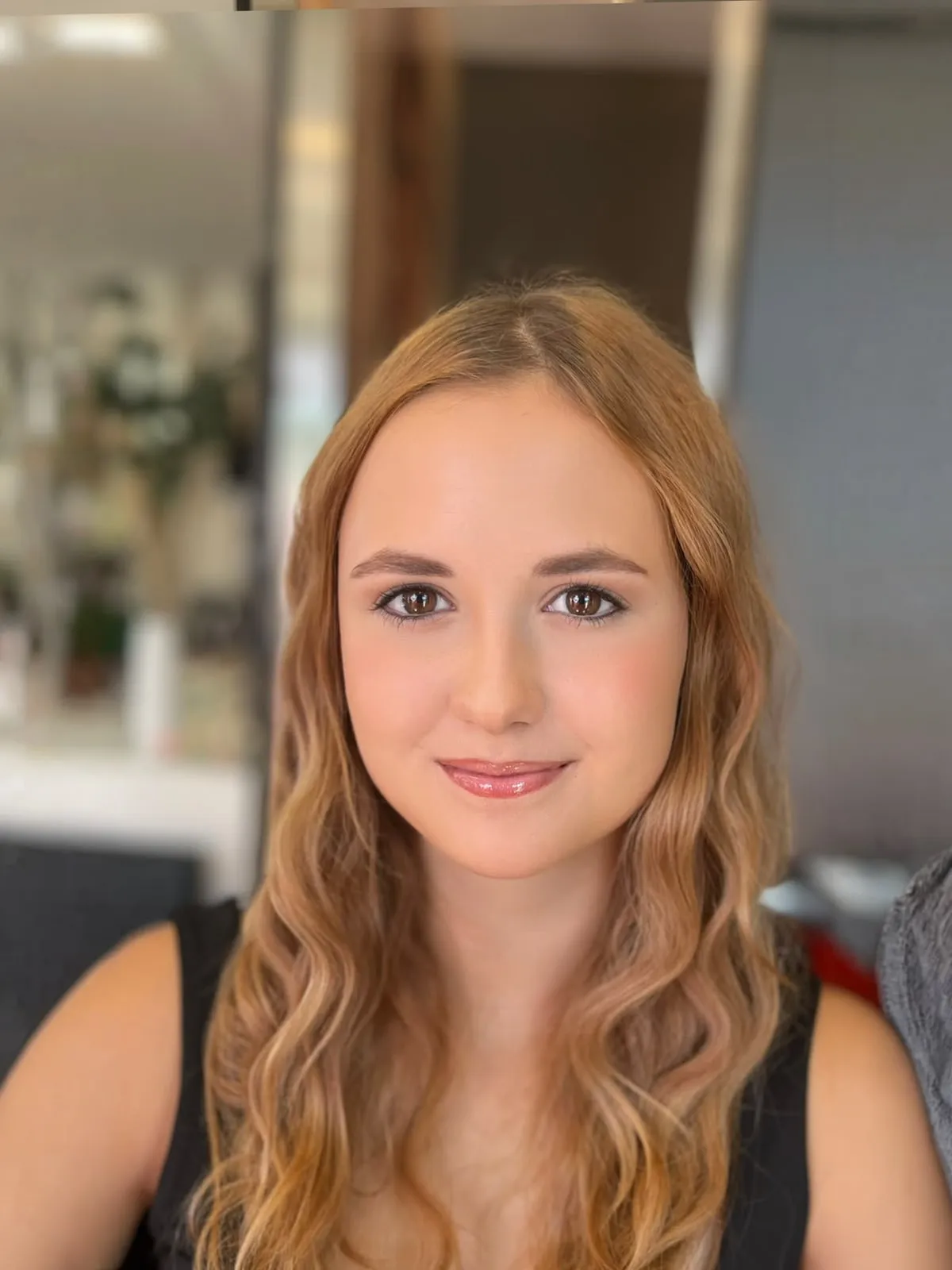 Dieselbe junge Frau mit Soft-Glam-Make-up: Gloss-Lippen, feiner Lidstrich und weiche Wellen