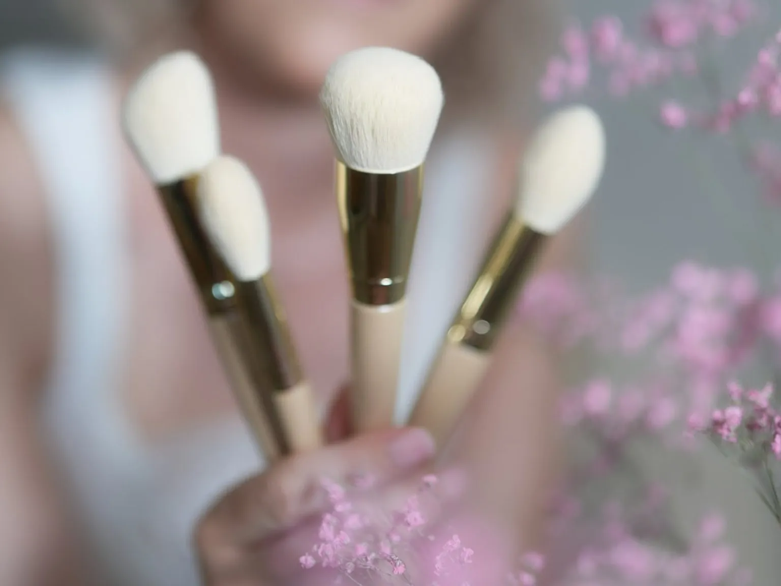 Christina hält vier Make-up-Pinsel in die Kamera, im Hintergrund rosa Schleierkraut